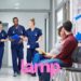 Pregnant woman and partner sitting in waiting area in hospital while three nurses walk down the corridor